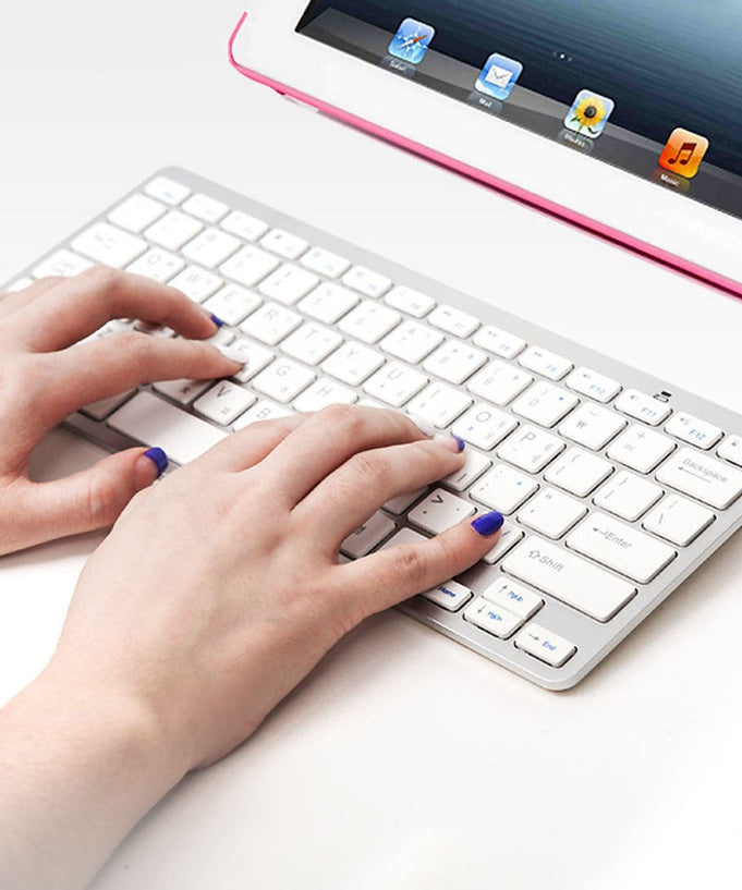 Hands typing on COSY Basic Silver Bluetooth Keyboard connected to a tablet, highlighting sleek design and wireless functionality.