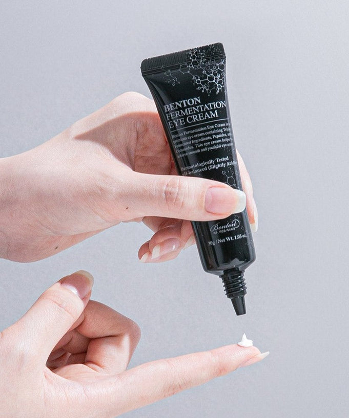 Person applying BENTON Fermentation Eye Cream 30ml, rich in peptides and ceramides, for anti-aging and elasticity around eyes.