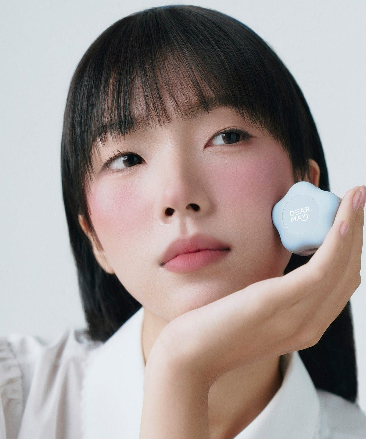 Person holding DEAR MAY Pure Falling Mood Lip Pot 6.5g with soft pink lips and rosy cheeks, showcasing makeup beauty.