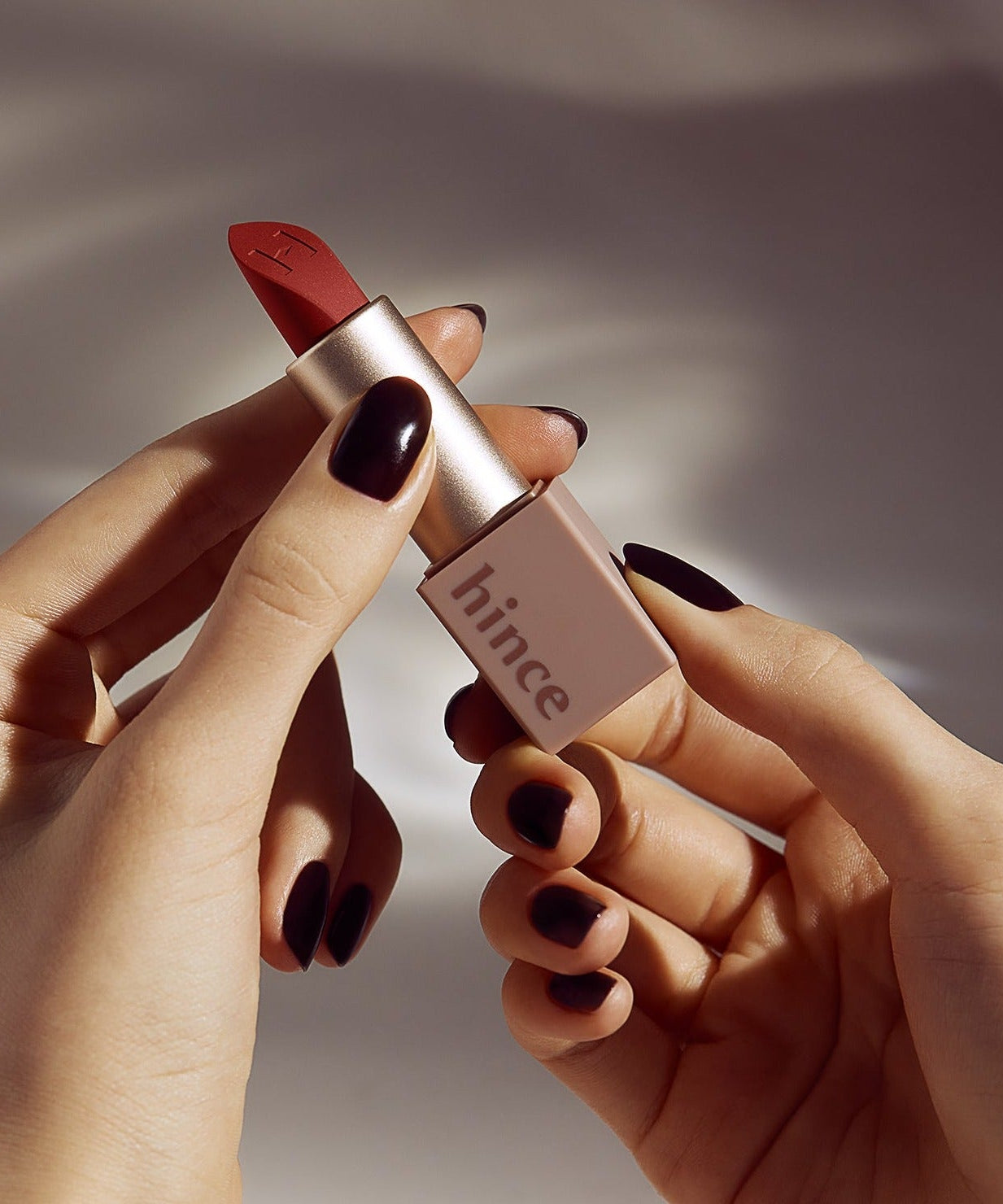 HINCE Mood Enhancer Matte lipstick held in hands with dark nail polish