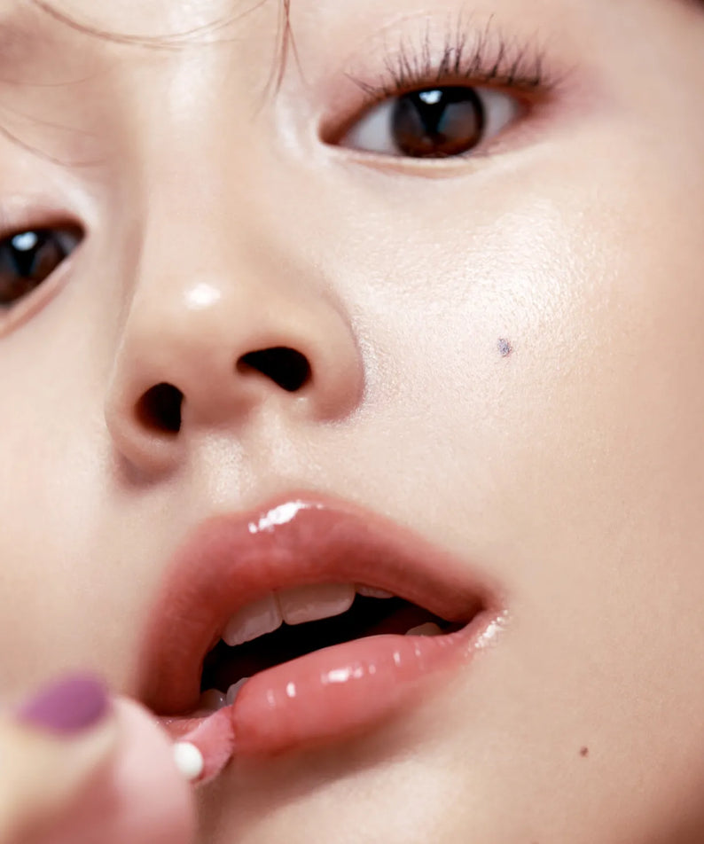 Close-up of a person applying FWEE 3D Voluming Gloss to lips for a shiny finish.