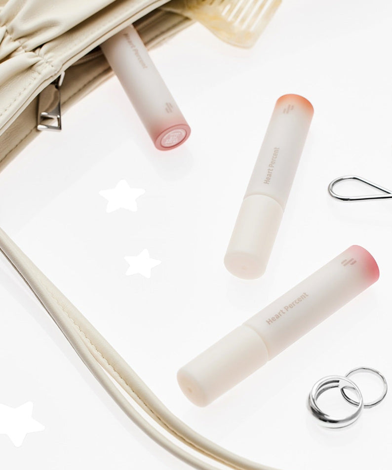 HEART PERCENT Dot On Mood All Cover Lip Base placed beside a purse and accessories on a white background.