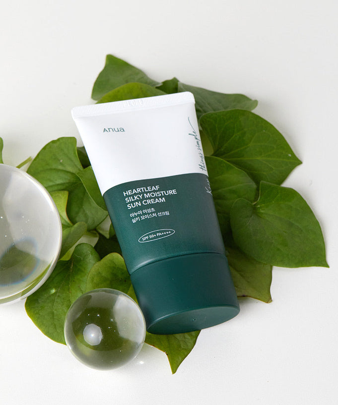 ANUA Heartleaf Silky Moisture Sun Cream 50ml displayed with green leaves and glass decor for skincare and sun protection.