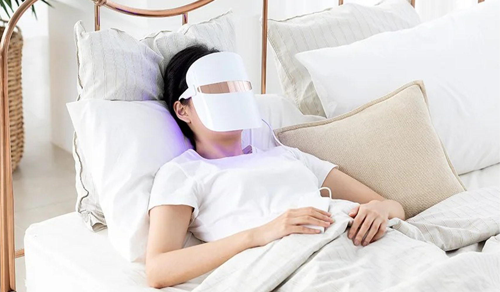 Person relaxing in bed using a LED light therapy mask for skincare treatment, enhancing skin health and relaxation.