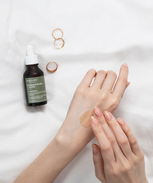 Applying MARY & MAY Houttuynia Cordata + Tea Tree Serum 30ml to skin with jewelry on bed