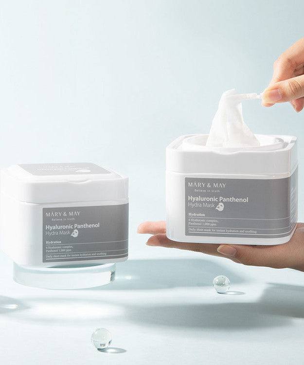 Person using MARY & MAY Hyaluronic Panthenol Hydra Mask x30 with product containers in the background