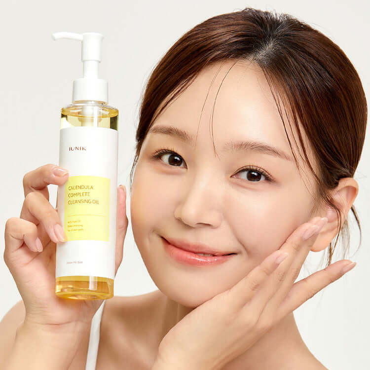 Woman holding iUNIK Calendula Complete Cleansing Oil 200ml bottle, showcasing skincare product.