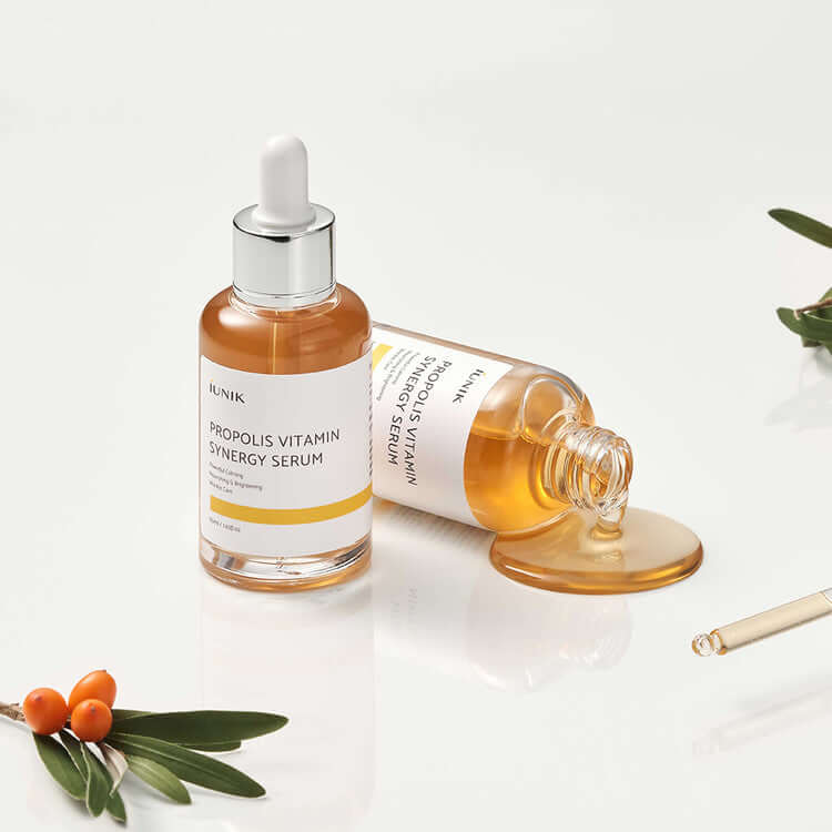 iUNIK Propolis Vitamin Synergy Serum 50ml bottle and spilled serum with green leaves and orange berries on white background