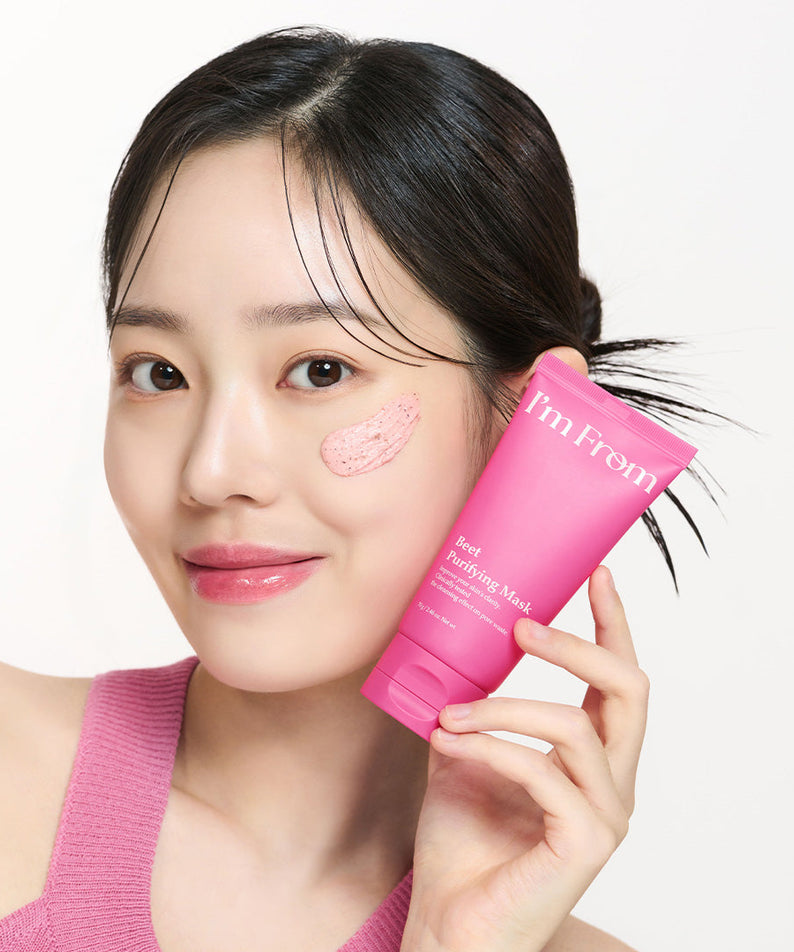 Woman holding I'M FROM Beet Purifying Mask 70g with product applied on cheek, showcasing skincare use.