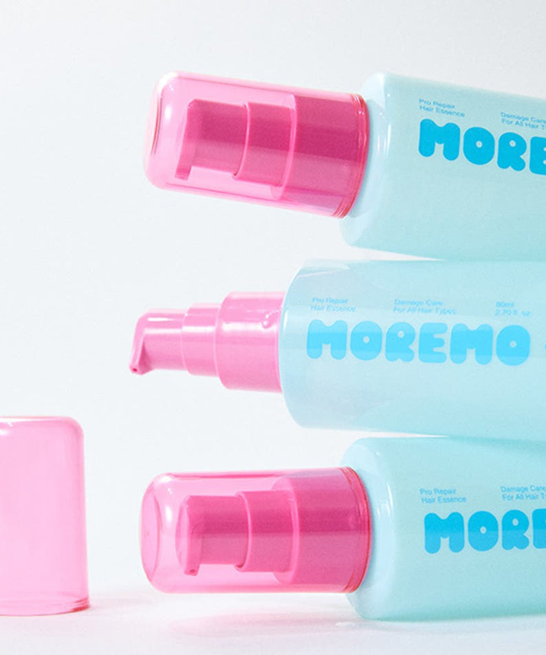 Three bottles of MOREMO Pro Repair Hair Essence with pink caps stacked on white background.