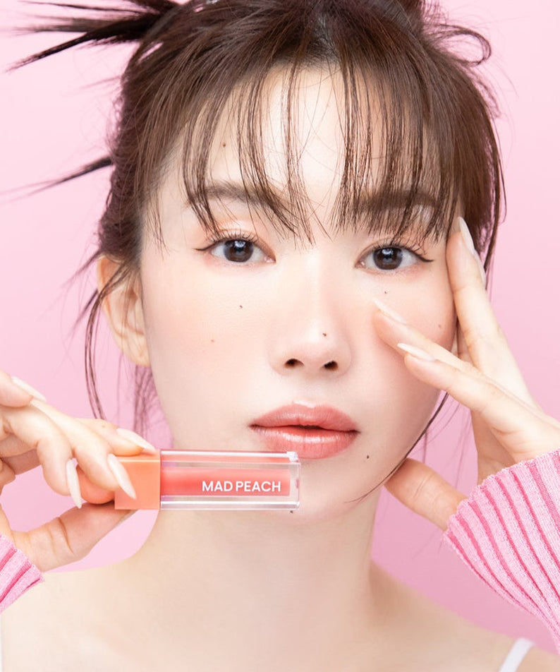 Woman holding IVI MAD PEACH Glow Fit Mood Gloss against pink background