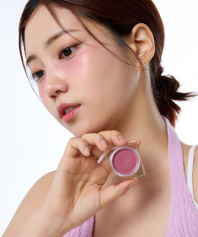Person posing with IVI MAD PEACH Mood Mix Cream Blusher applied on cheeks, holding the product in hand.