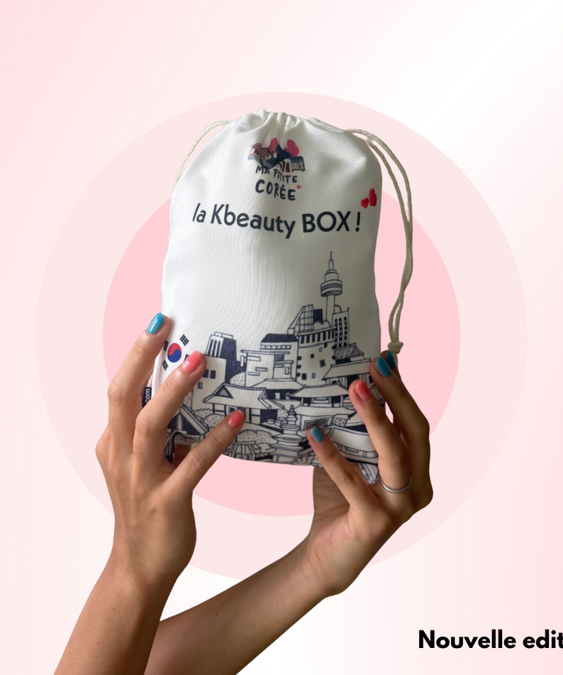 Hands holding La K-beauty Box - Nouvelle edition against a pink background with city illustration on the box.