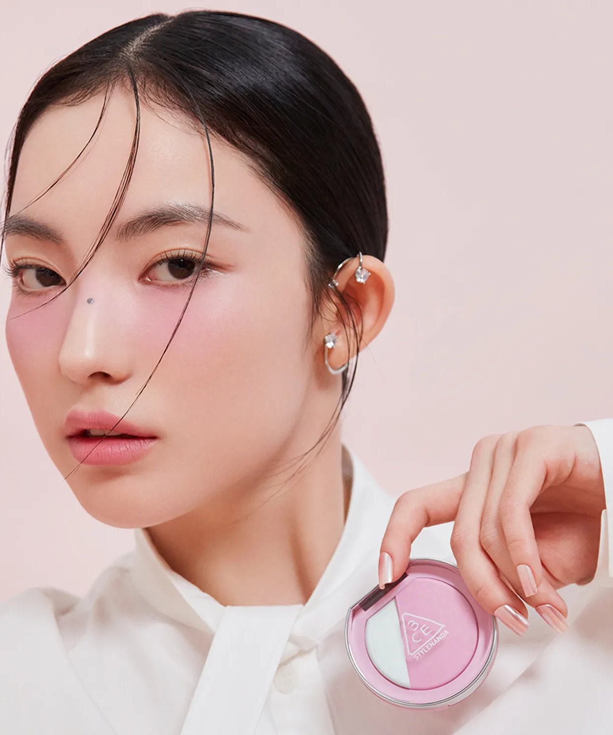 Model displaying 3CE Blushlighter on cheeks with product in hand, demonstrating vibrant and stylish makeup look.