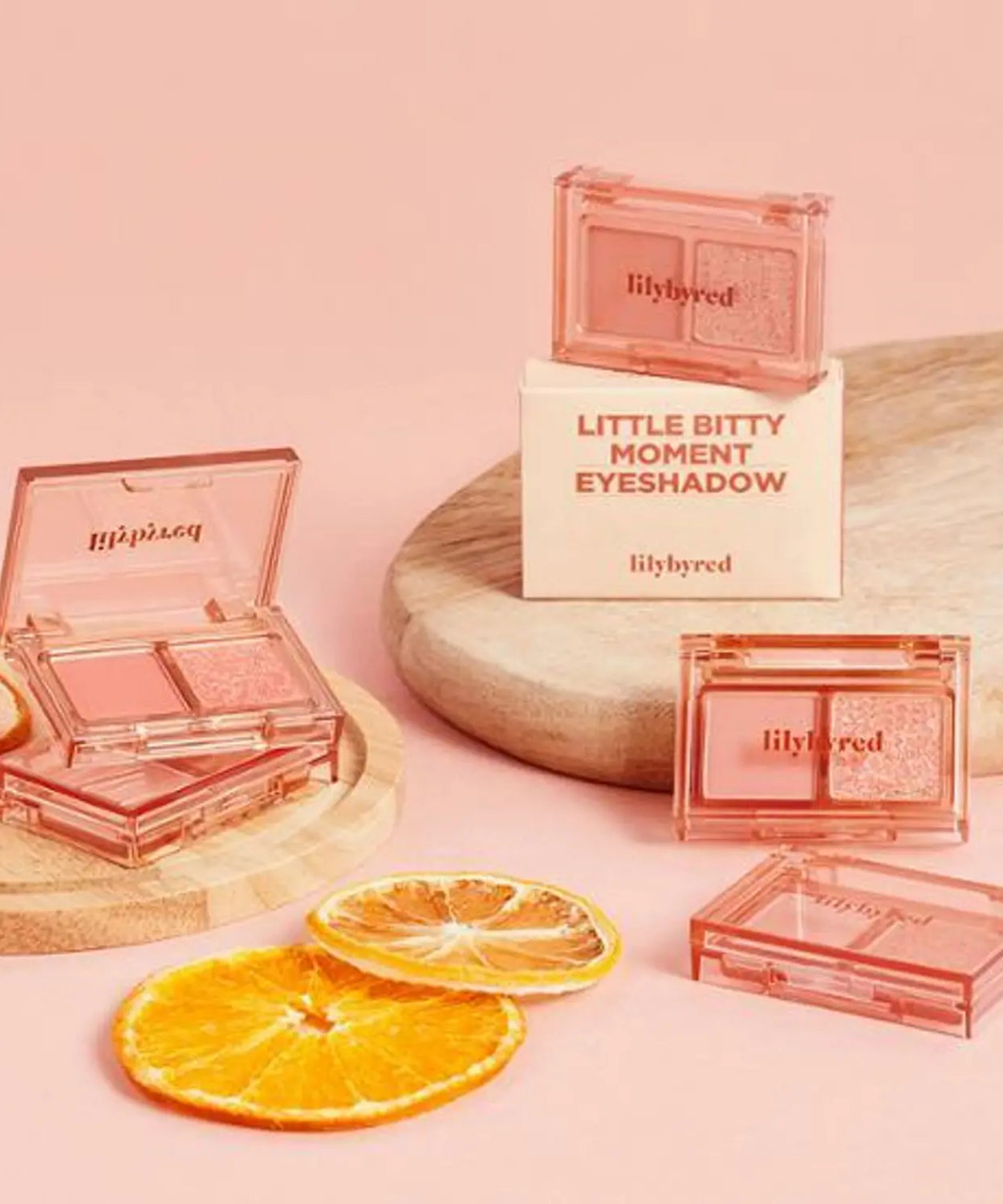 LILYBYRED Little Bitty Moment Shadow in pink packaging on a wooden tray with citrus slices, enhancing any makeup collection.