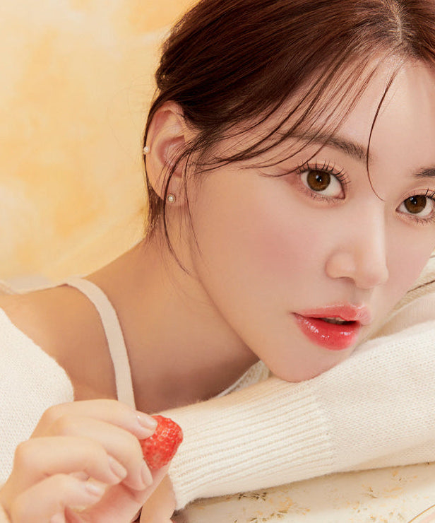 Woman holding a strawberry, showcasing natural beauty with soft lighting and a serene expression.