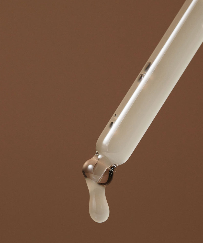 Droplet emerging from a pipette containing AROMATICA Vitalizing Rosemary Elasticity Ampoule 30ML on a brown background.