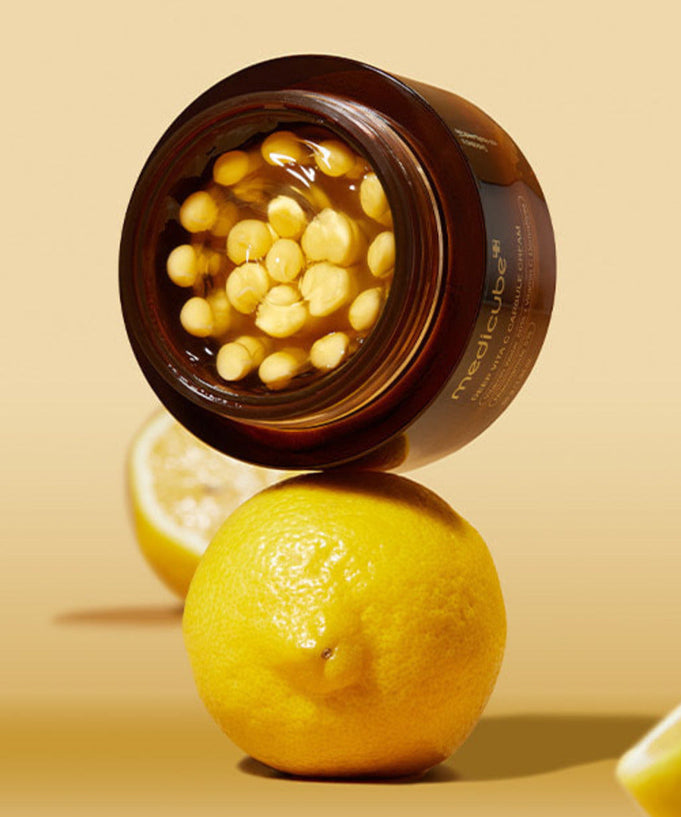 Open jar of MEDICUBE Deep Vita C Capsule Cream 55g with lemons in the background, showcasing skincare product ingredients.