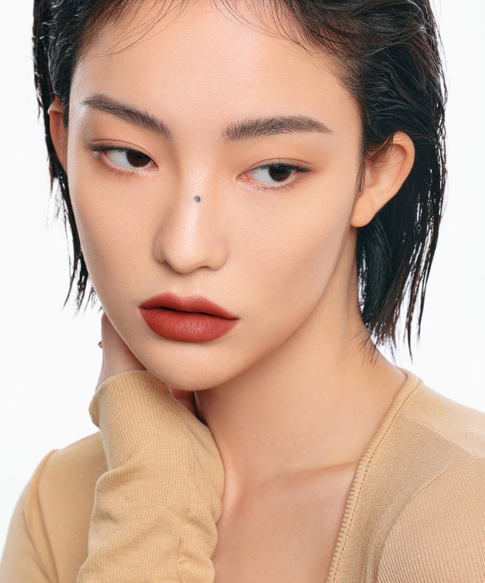 Portrait of a woman with natural makeup and short dark hair, wearing a beige top.