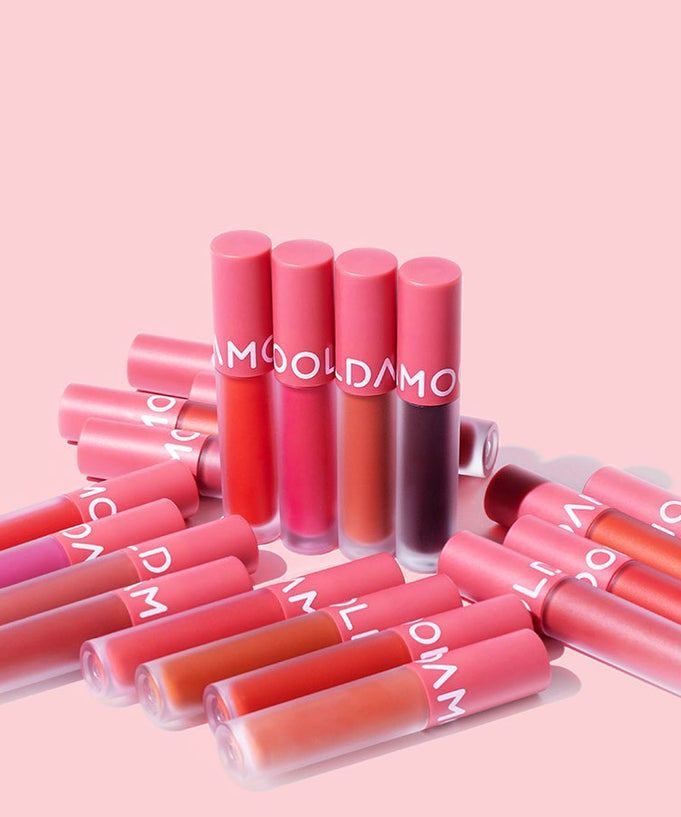 MOOLDA Tattoo Fixing Lip Tint collection in various shades of pink and red on a pink background.