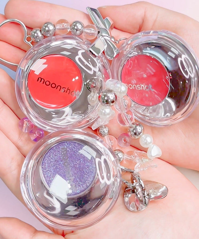 Hand holding colorful MOONSHOT Melting Mood Lip & Cheek products with playful design and vibrant shades for lips and cheeks.