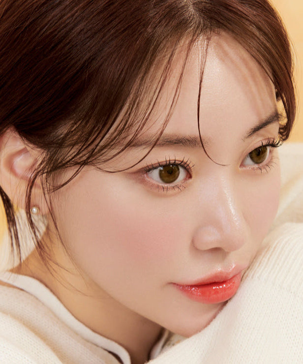 Close-up of a person with brown hair and warm skin tone, wearing a white sweater and pearl earrings, gazing thoughtfully.