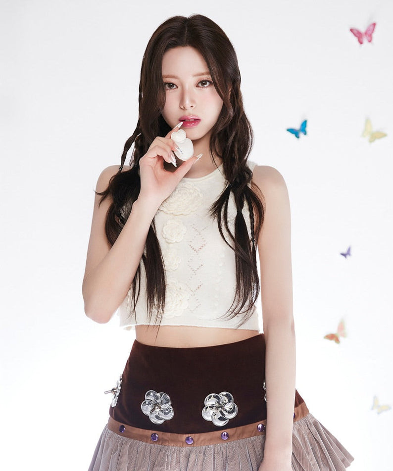 Woman holding a flower with colorful butterflies in the background, dressed in a white top and brown skirt. NAMING Glow Heart Lip Tint beauty.