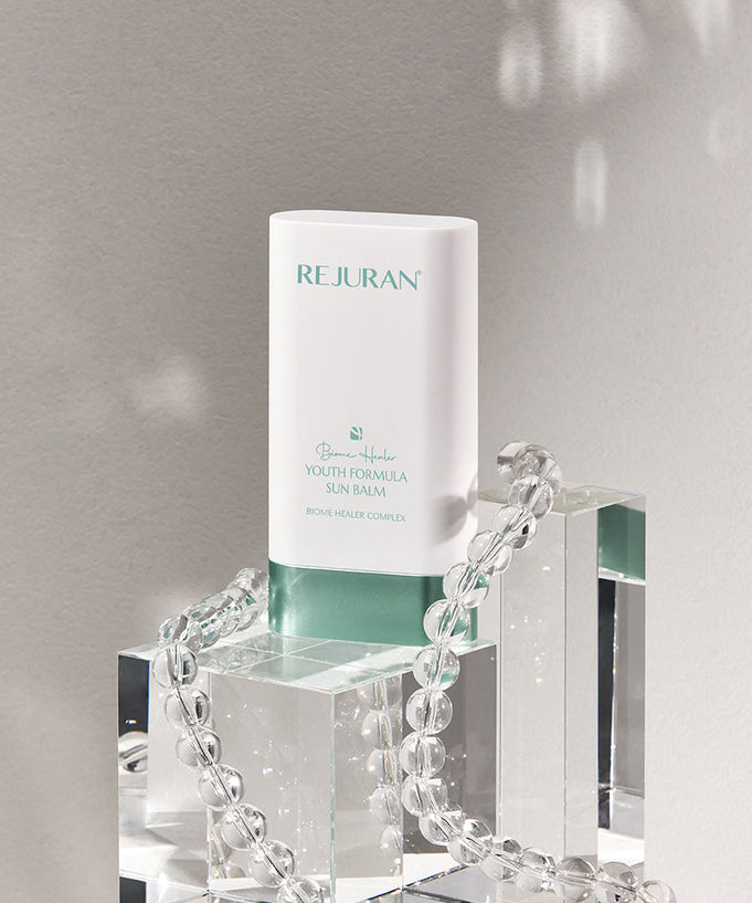 REJURAN Biome Healer Youth Formula Sun balm 19g displayed on glass blocks with decorative beads.