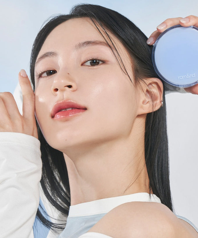 Model holding ROMAND bare water cushion in hand, showcasing fresh and natural skin look with compact design.