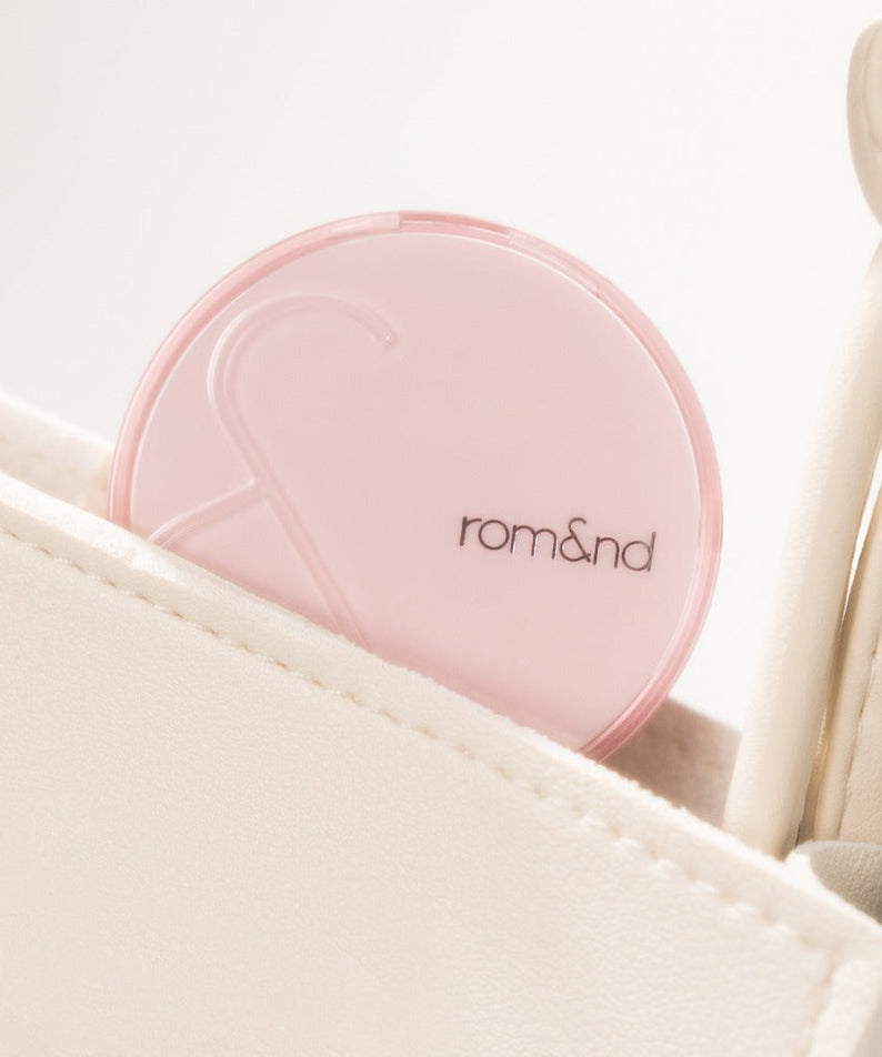 ROMAND Bloom in Coverfit Cushion mini in a light pink compact, placed inside a beige bag, showcasing its travel-friendly design.