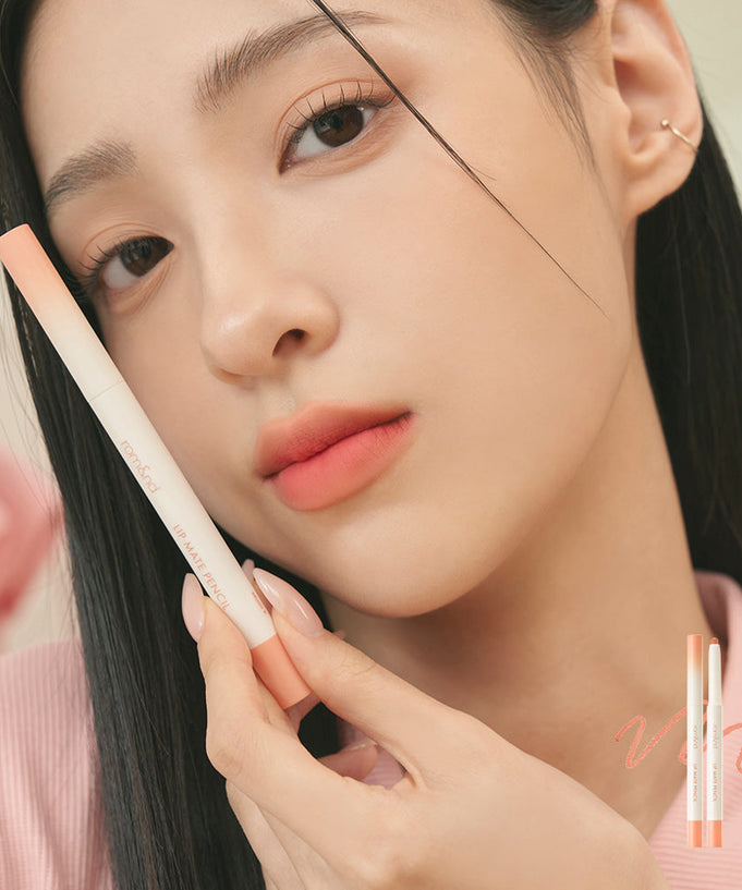 Woman holding ROMAND lip mate pencil #beovershade, showcasing soft peach lip color and smooth texture with elegant design.