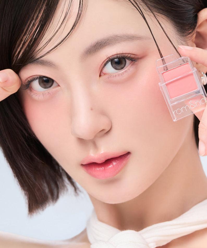 Woman holding ROMAND Slide In Single blush compact near her face, highlighting natural makeup look