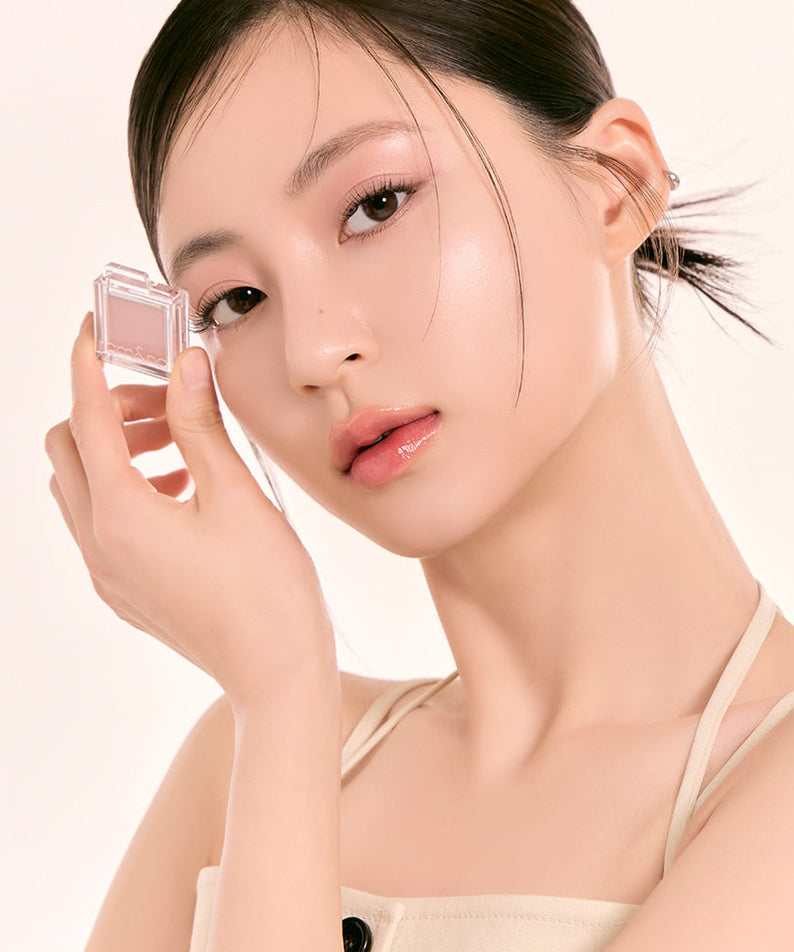 Model holding ROMAND Slide In Single #mattepearl makeup product next to her face