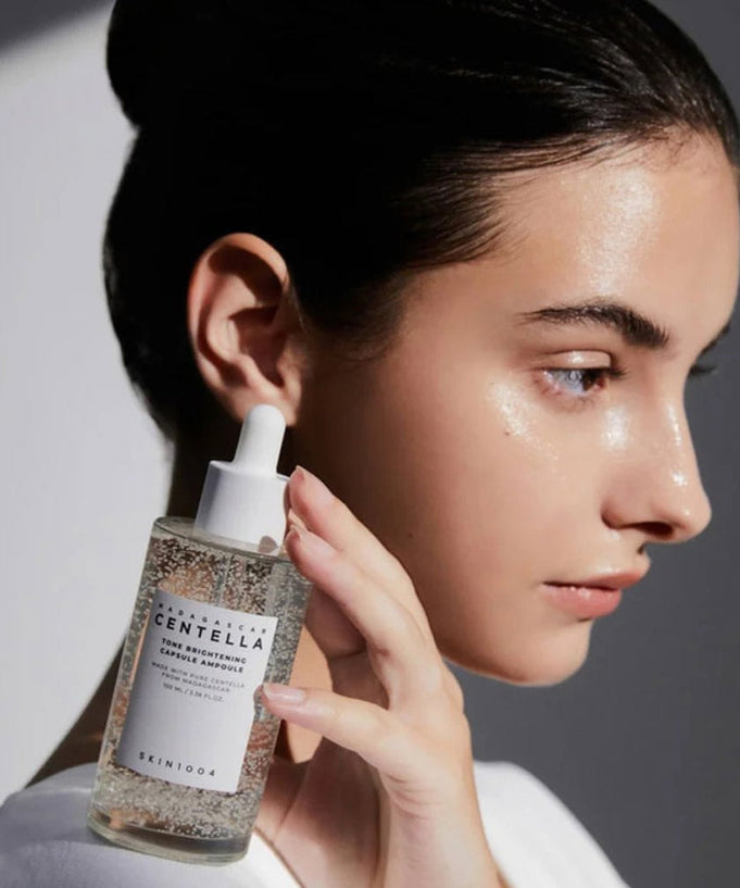 Person holding SKIN1004 Madagascar Centella Tone Brightening Capsule Ampoule 100ml next to face