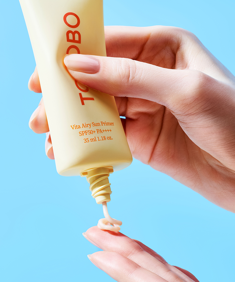 Applying TOCOBO Vita Airy Sun Primer 35ml on hand with blue background for skincare routine