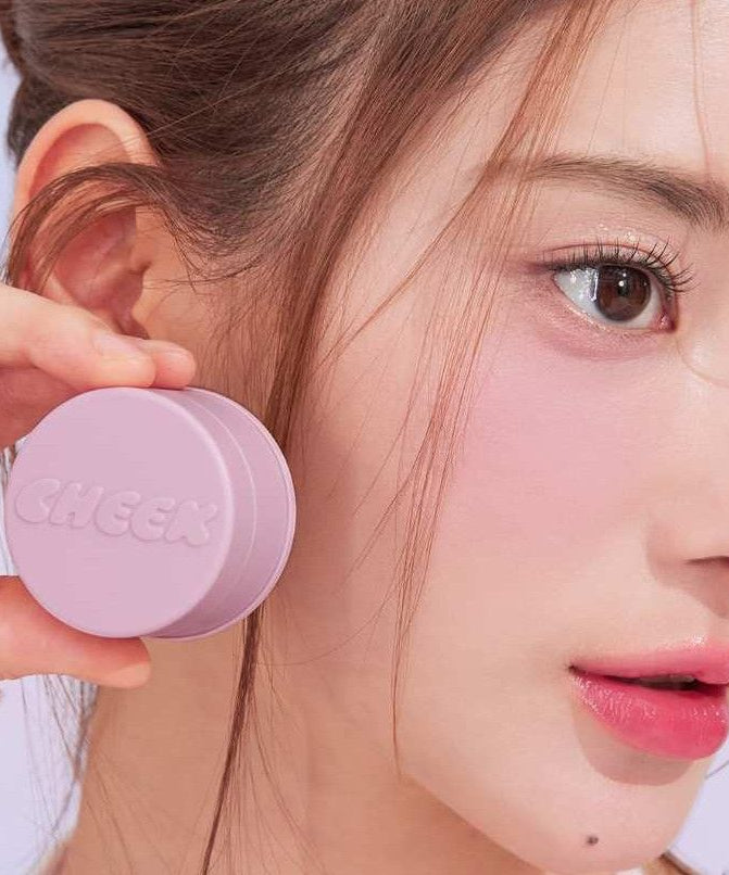 Woman holding TONY MOLY Cheektone Jelly Blusher next to her face showcasing the product's texture and color.