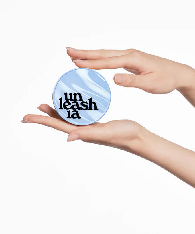 Hands holding UNLEASHIA Babe Skin Baby Blue Cushion compact makeup product with stylish packaging.