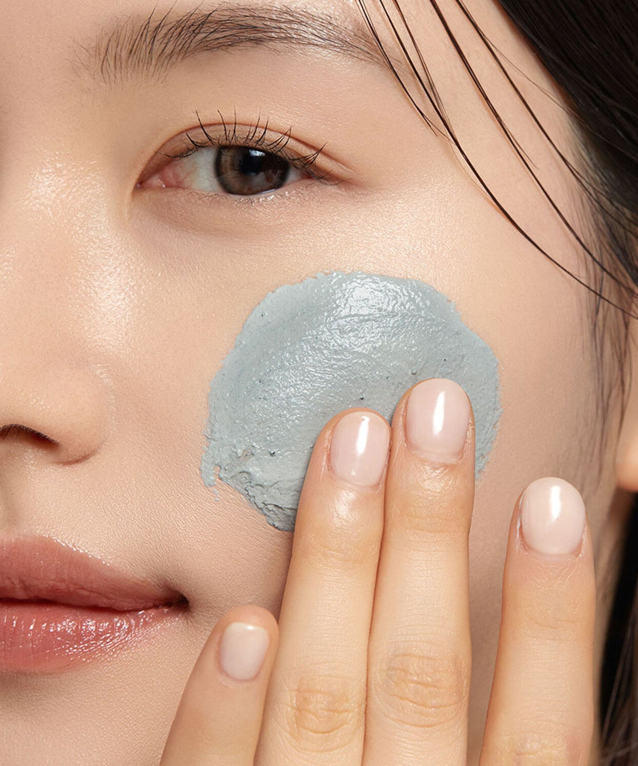 Woman applying WHIPPED Mugtree Vegan Cookie Clay Pack Cleanser 180ml on her cheek for skincare routine.